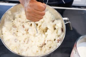 hand mashing potatoes in silver bowl