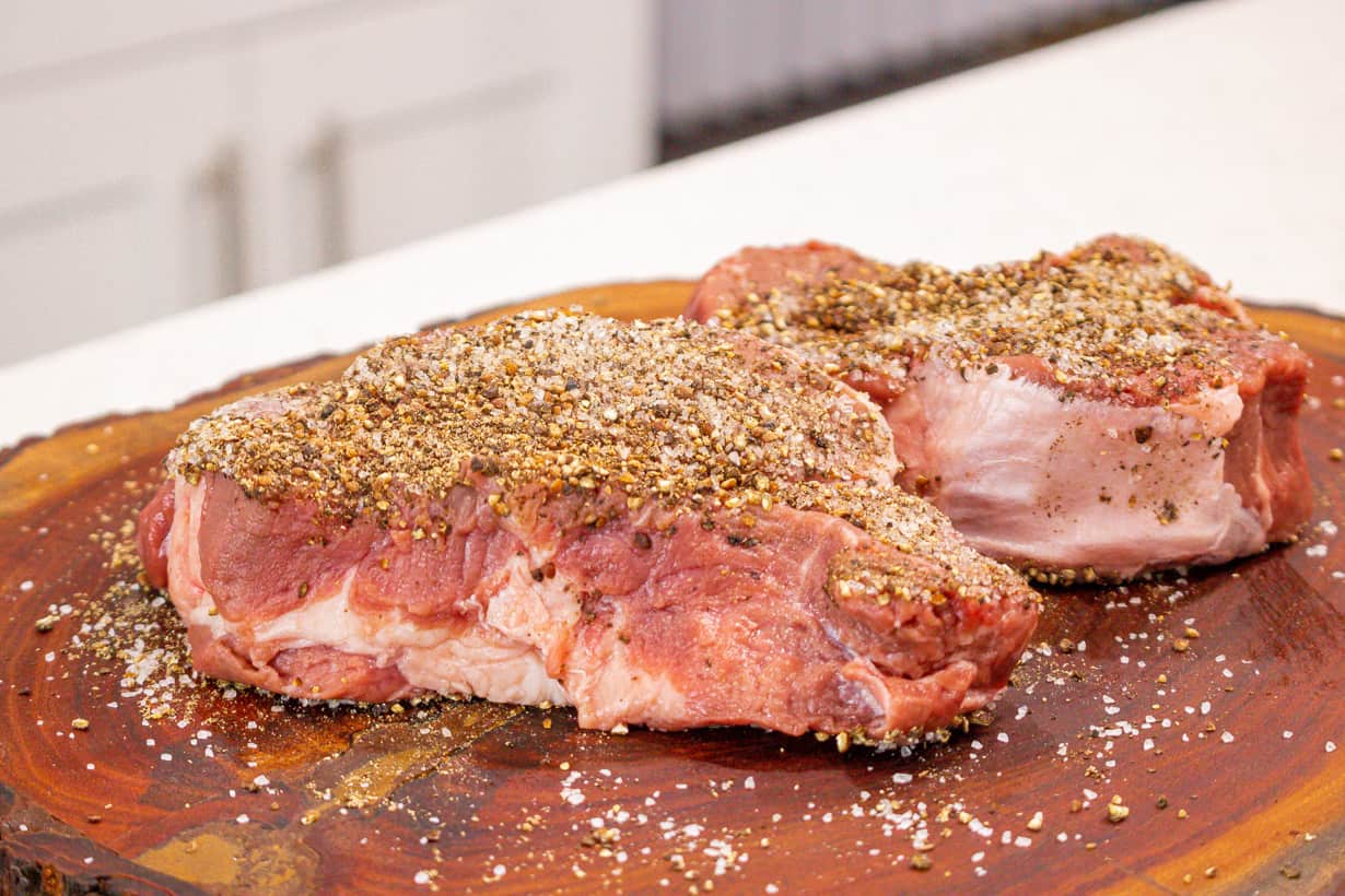 seasoned steak with pepper on top of wooden board