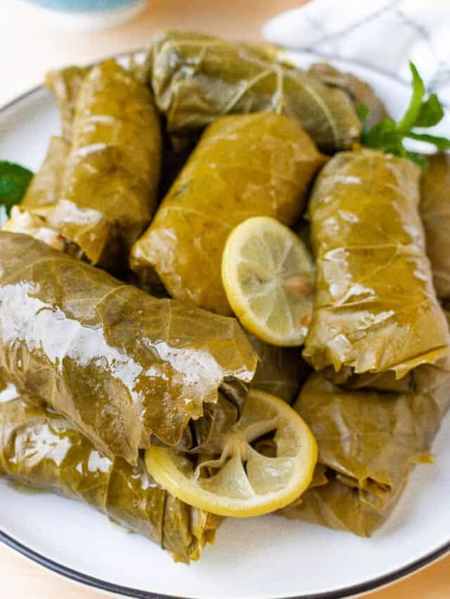 stacked grape leaves with lemon slices on white plate