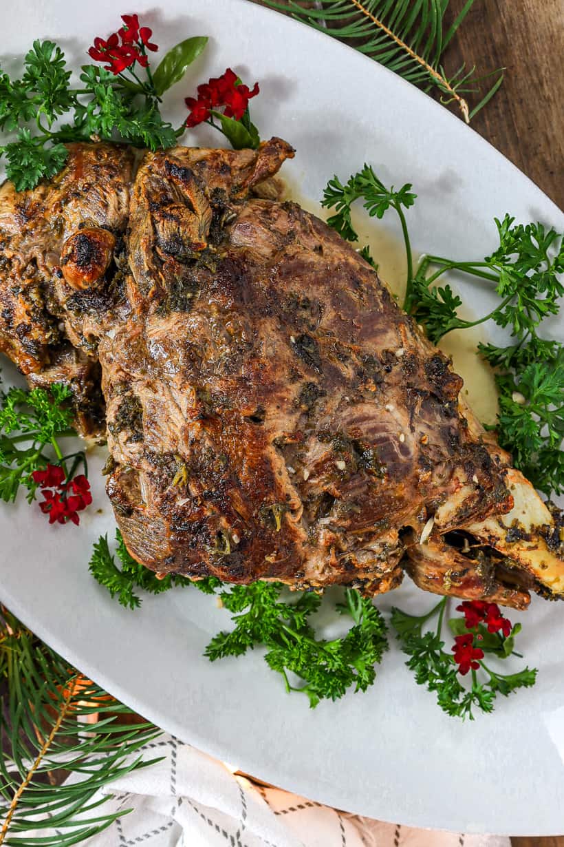 Bone in Leg of lamb on white plate with red flowers and fresh herbs