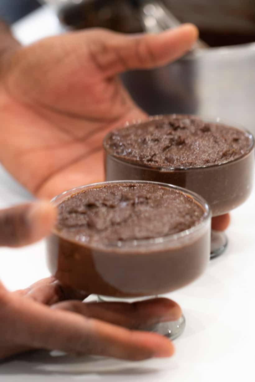 hands holding chocolate mousse in glasses