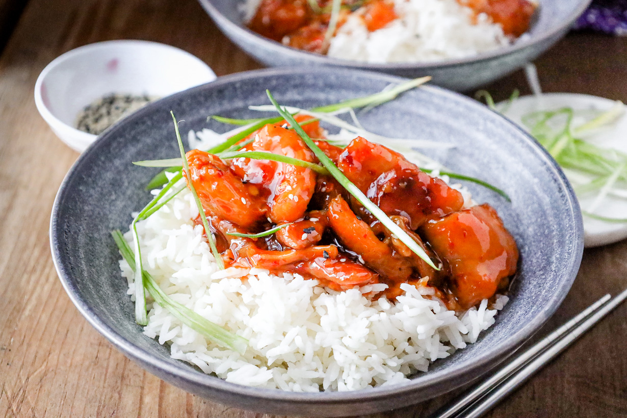 Firecracker chicken on top of rice with green onions.