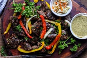 Steak bites on wooden board with herbs and peppers