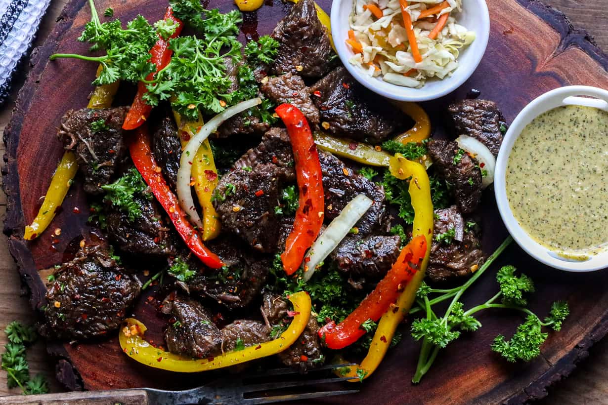 Steak bites on wooden board with herbs and peppers