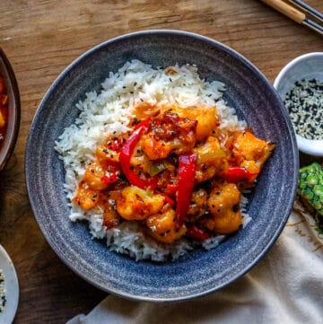 sweet and sour cauliflower over white topped with sesame seeds and bell peppers