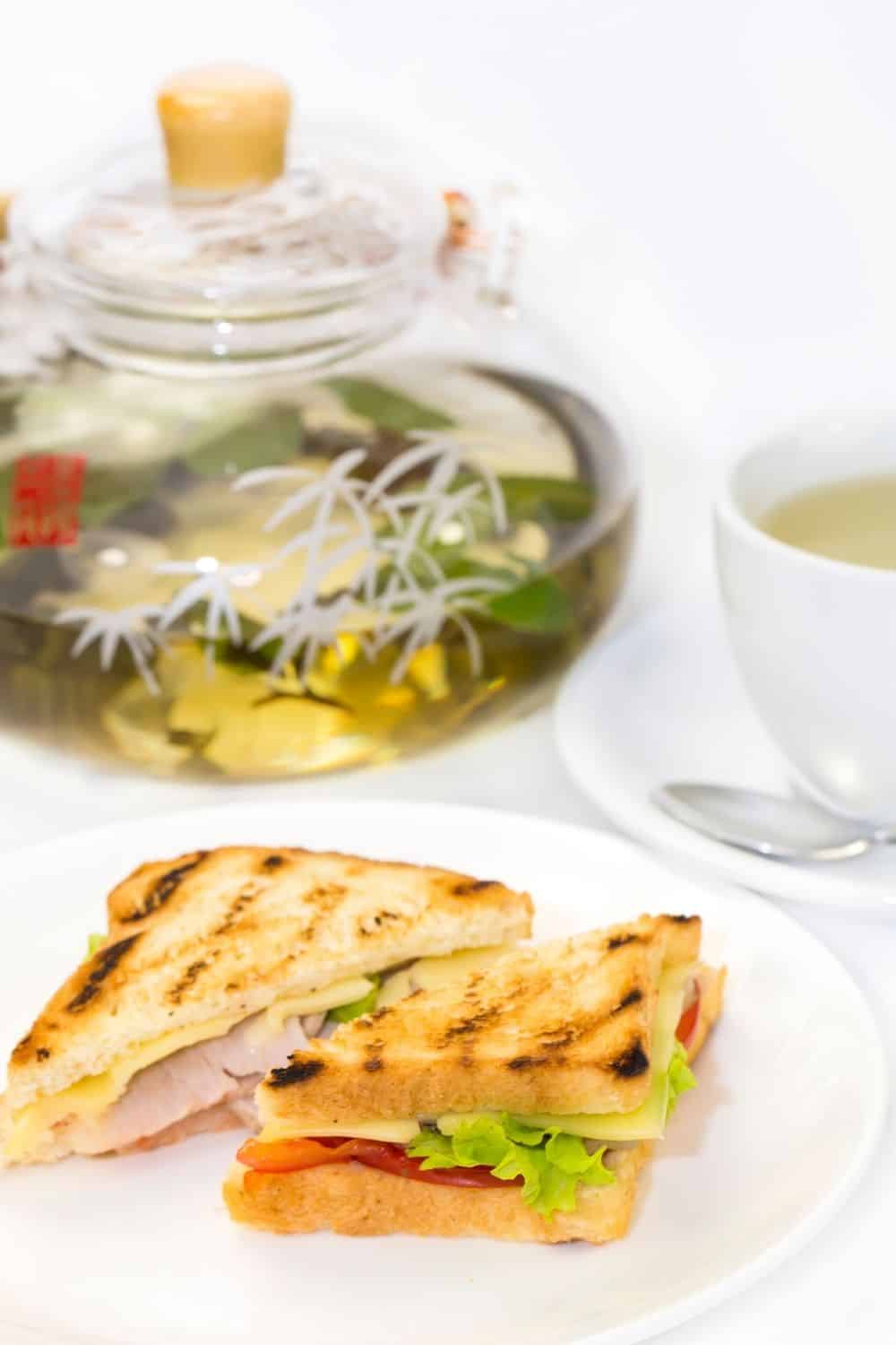 sandwich on white plate with tea in the background