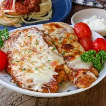 parmesan chicken with tomatoes on white plate and parsley