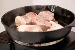 Searing the meat in a skillet.