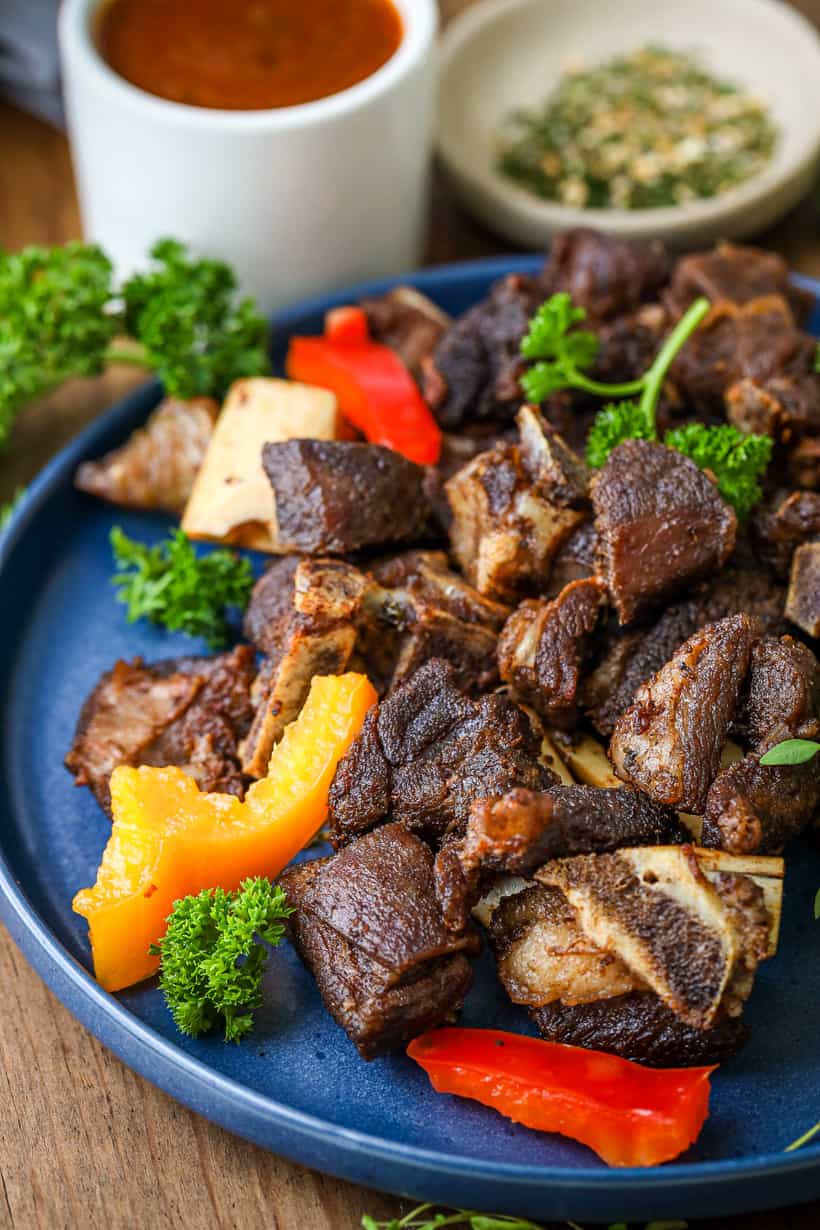 Goat meat pieces on blue plate with herbs