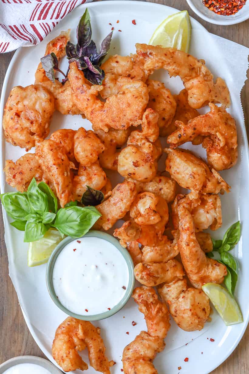 tempura shrimp on white plate with sauce and herbs
