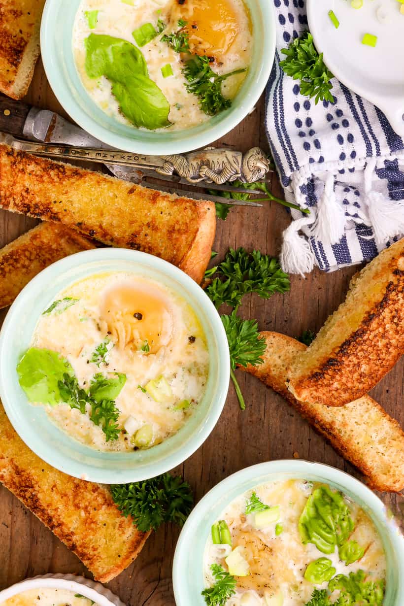 Oven baked eggs in ramekins and bread on wooden board