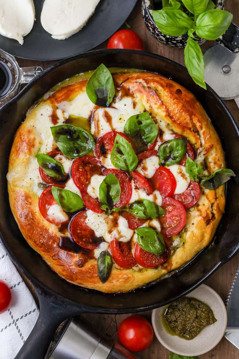 Caprese pizza in cast iron skillet on wooden board with herbs