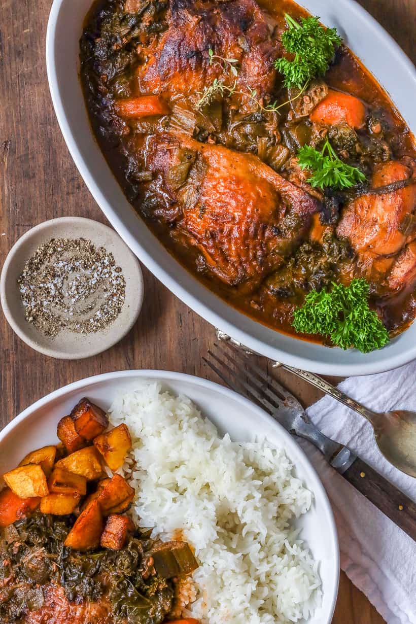 kale stew in bowl with chicken and fresh herbs with rice and fried plantains in the background