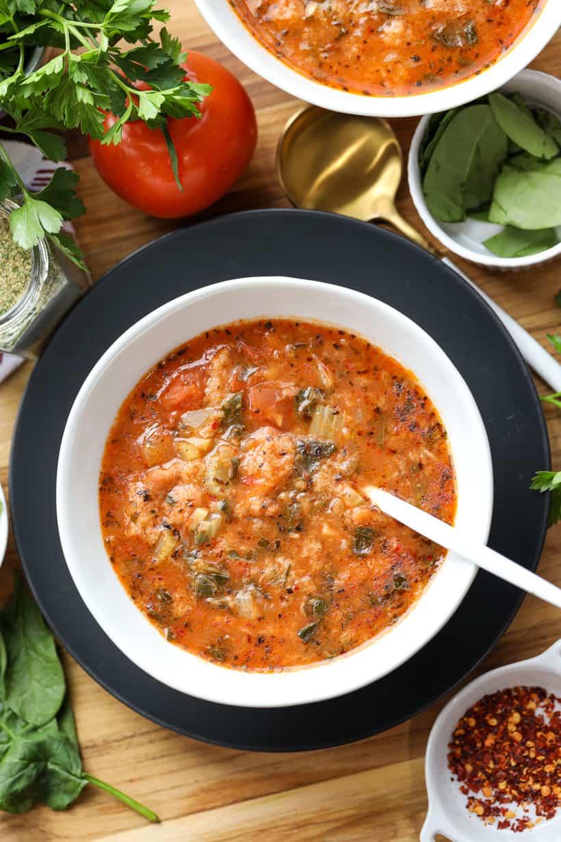 Soup with spoon in white bowl with tomato and herbs