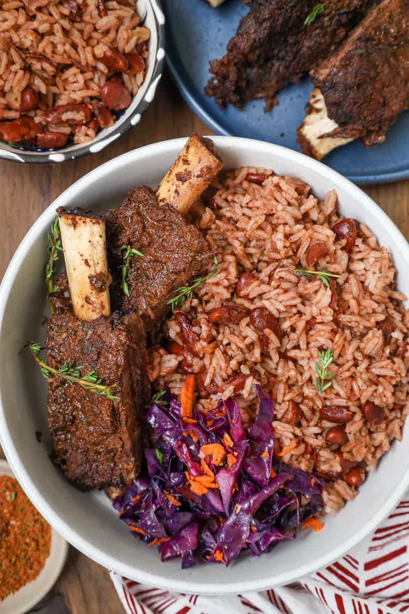 jerk ribs on white plate with herbs, rice and red beans and cabbage salad