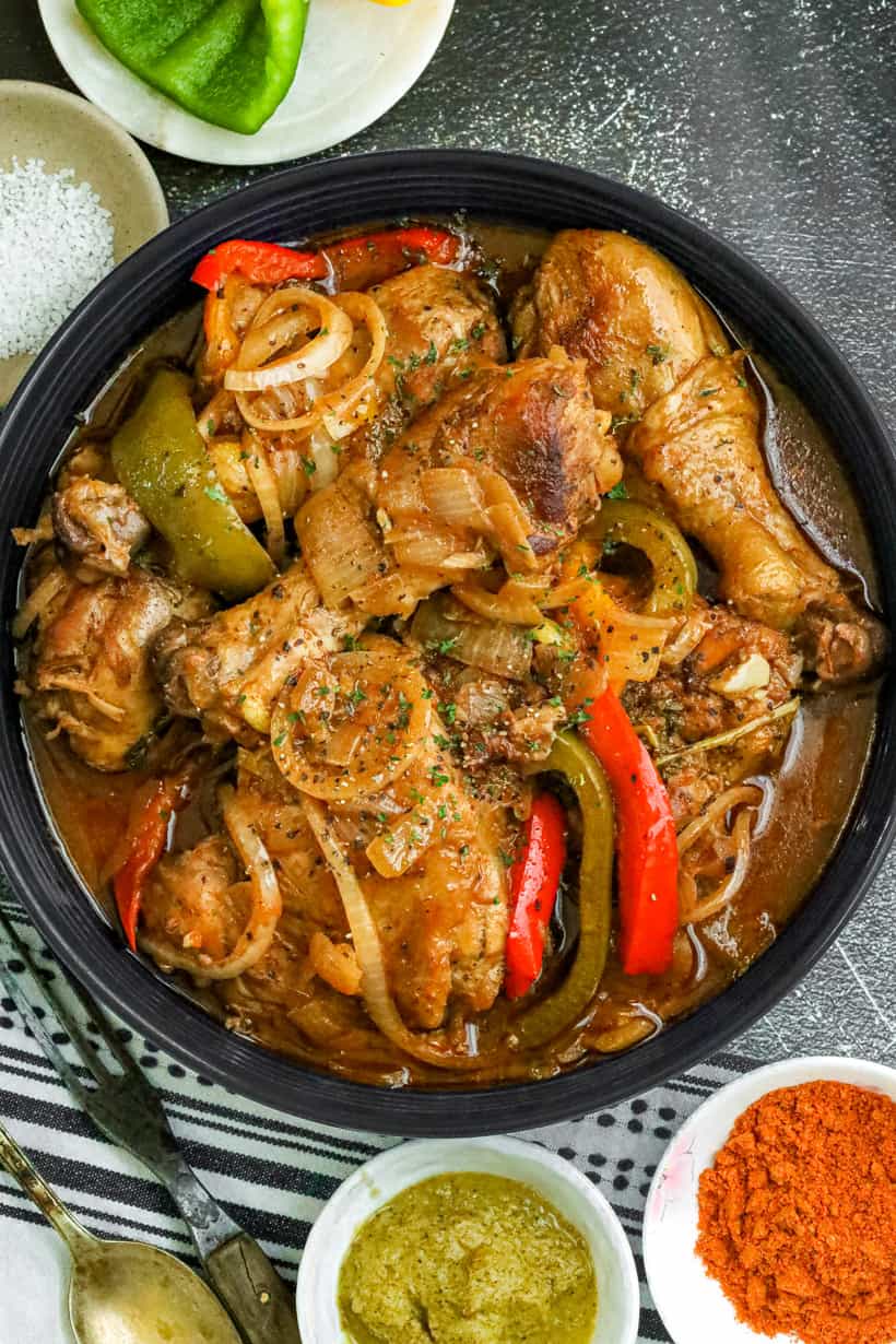 Poulet en sauce (Haitian Chicken Stew) in a bowl topped with onions and sweet peppers