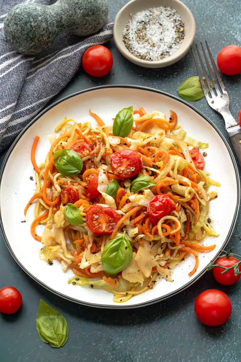 Veggie Spaghetti on a white plate topped with fresh basil and cherry tomatoes.