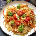 Veggie Spaghetti on a white plate topped with fresh basil and cherry tomatoes.