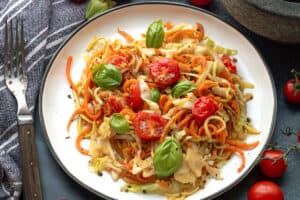 Veggie Spaghetti on a white plate topped with fresh basil and cherry tomatoes.