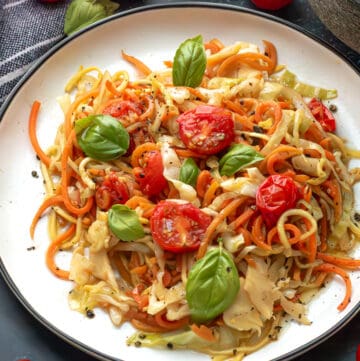 Veggie Spaghetti on a white plate topped with fresh basil and cherry tomatoes.