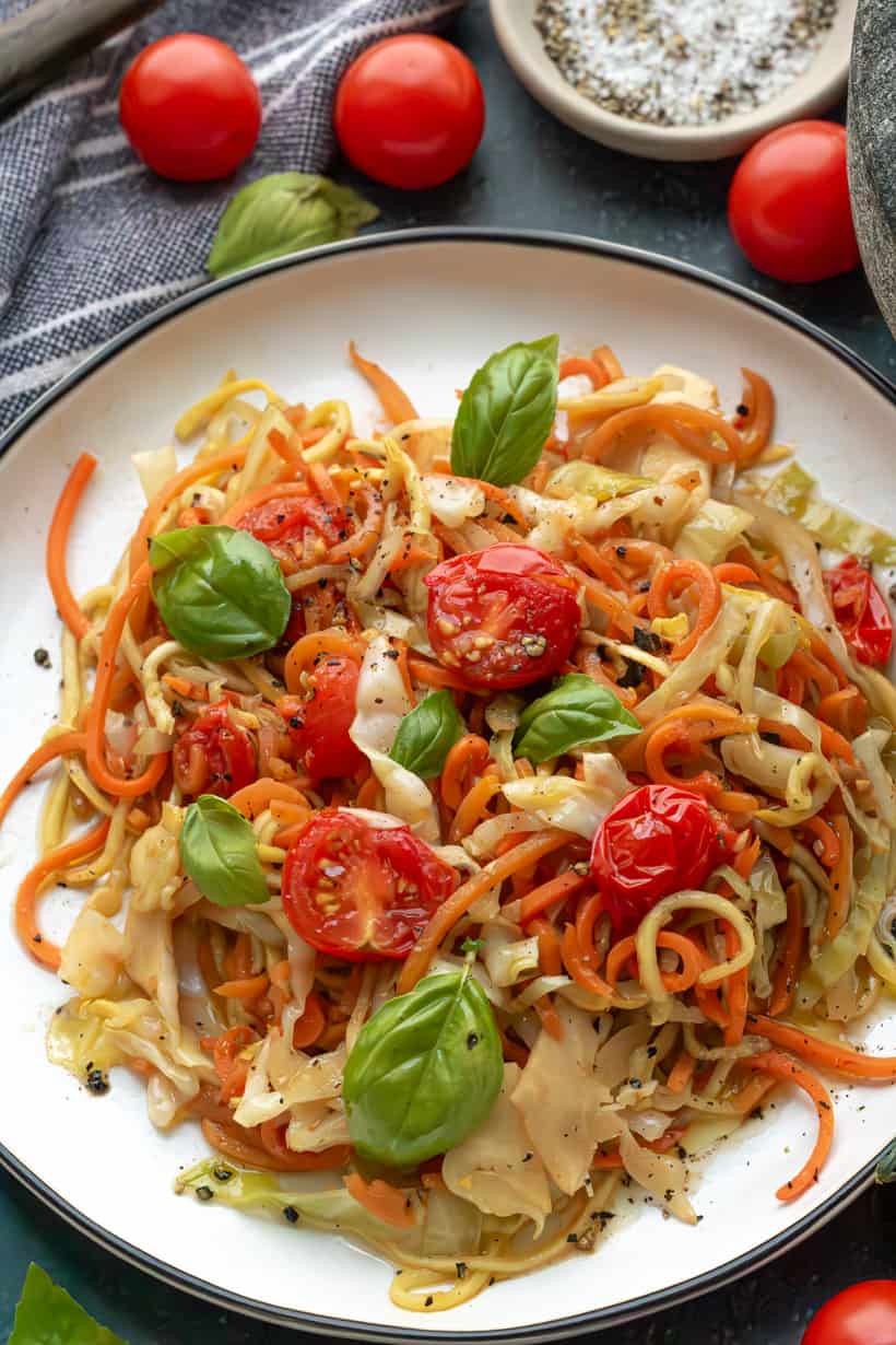 Veggie Spaghetti on a white plate topped with fresh basil and cherry tomatoes.