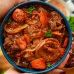 hands holding Haitian stew in blue bowl.