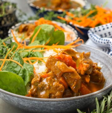 Curry goat in bowl with rice and vegetables