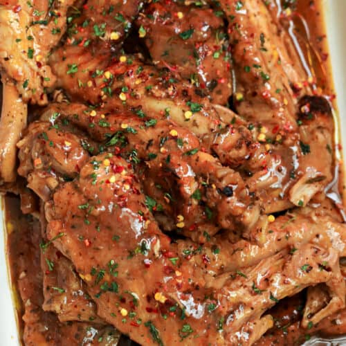Smothered turkey wings in baking dish topped with red pepper flakes and dried parsley over a bed of rice