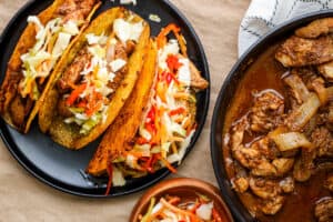 3 tacos with Haitian style chicken on black plate and topped with pikliz.