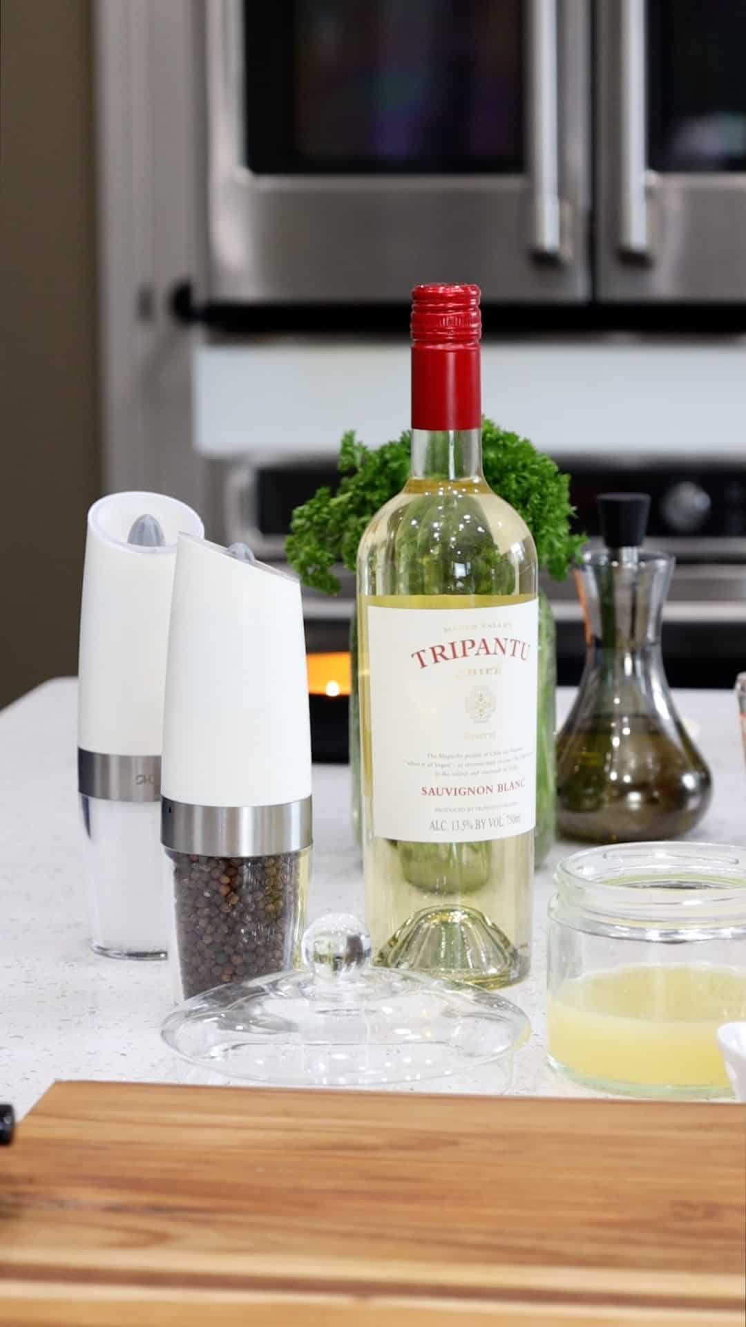 Sauvignon Blanc on the kitchen counter with bottle of olive oil, salt and pepper in grinder, lemon juice in glass jar.