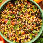 Cowboy caviar / Texas Caviar in green bowl surrounded by chips, lime, pepper, and herbs.