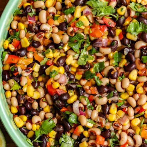 Cowboy caviar / Texas Caviar in green bowl surrounded by chips, lime, pepper, and herbs.