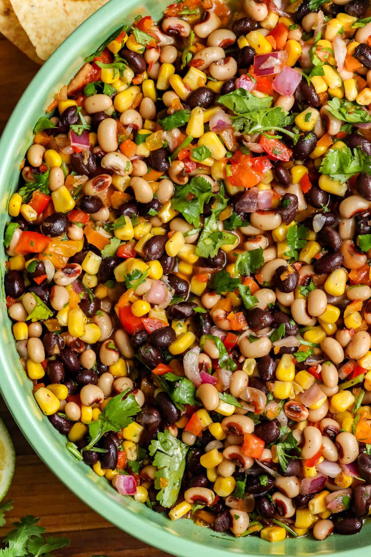 Cowboy caviar / Texas Caviar in green bowl surrounded by chips, lime, pepper, and herbs.