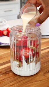 adding milk to strawberries, yogurt, flaxseed in blender