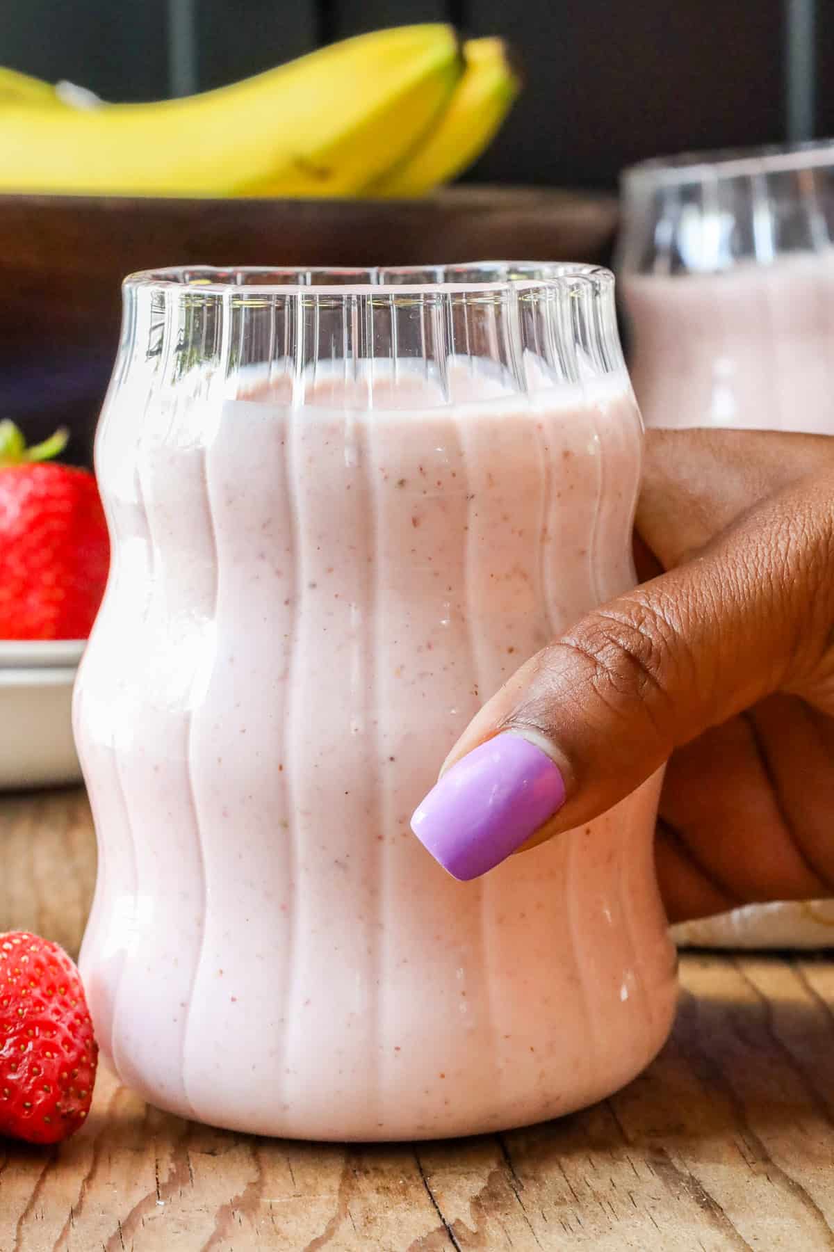 Hand holding glass filled with breakfast smoothie prepared with fresh strawberries and bananas.