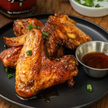 Chipotle Chicken Wings on black plate with sauce and topped with chives