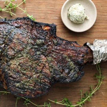 Grilled Cowboy Steak on wooden board with herb butter and herbs on the side