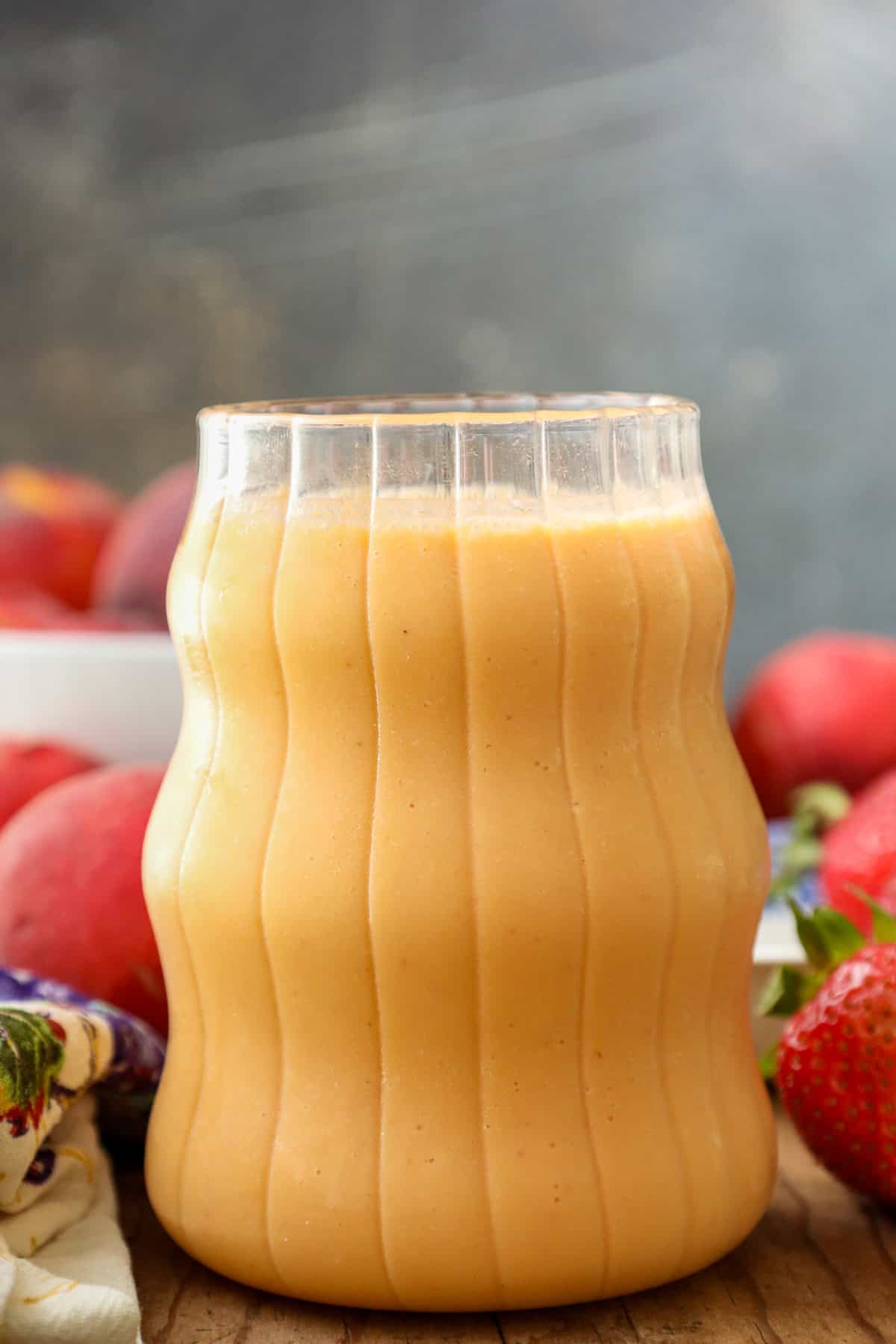 Strawberry Peach Smoothie in clear glass with strawberries and peach on a wooden board