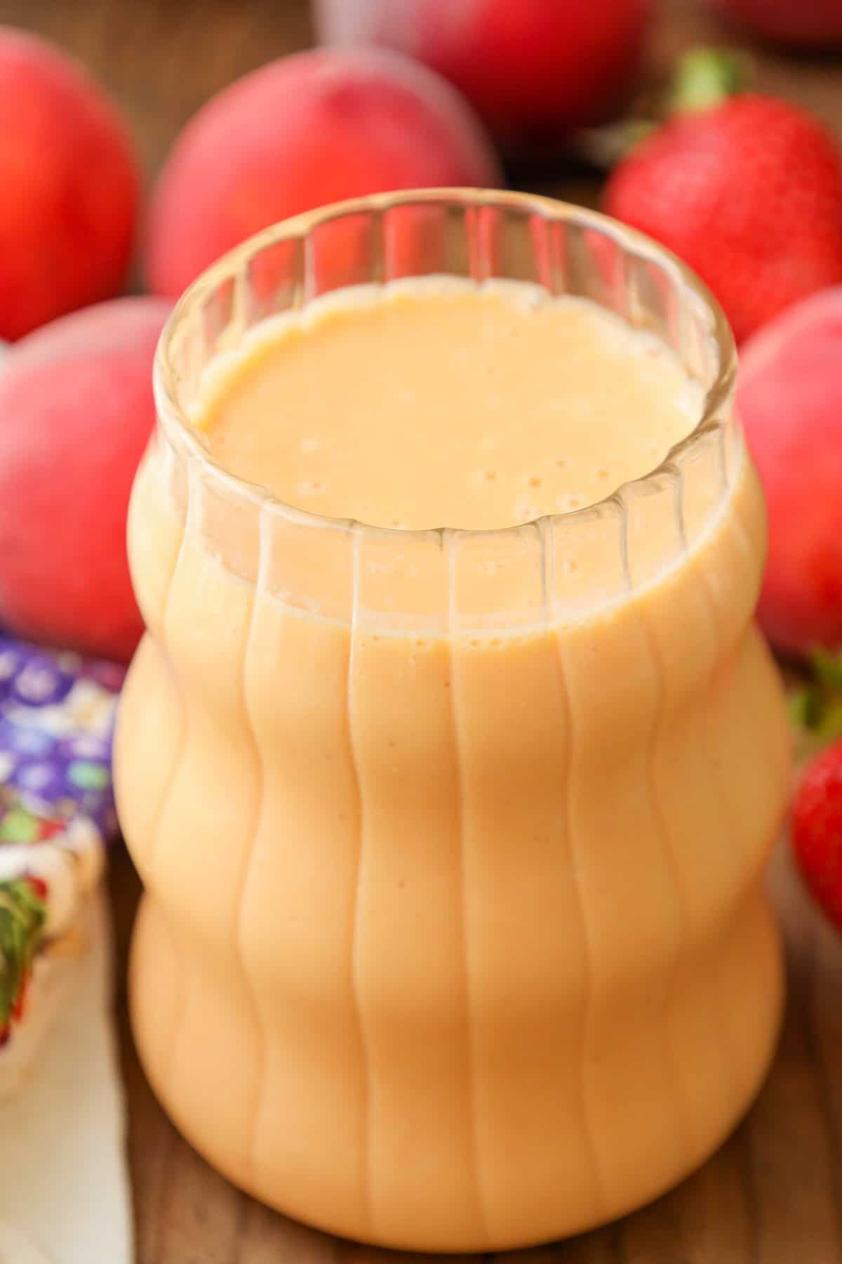 Strawberry Peach Smoothie in clear glass with strawberries and peach on a wooden board