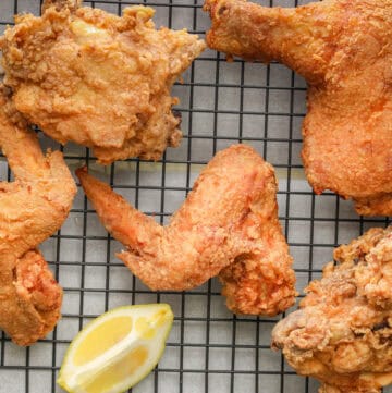 Louisiana Fried Chicken on a cooling rack with lemon wedges.
