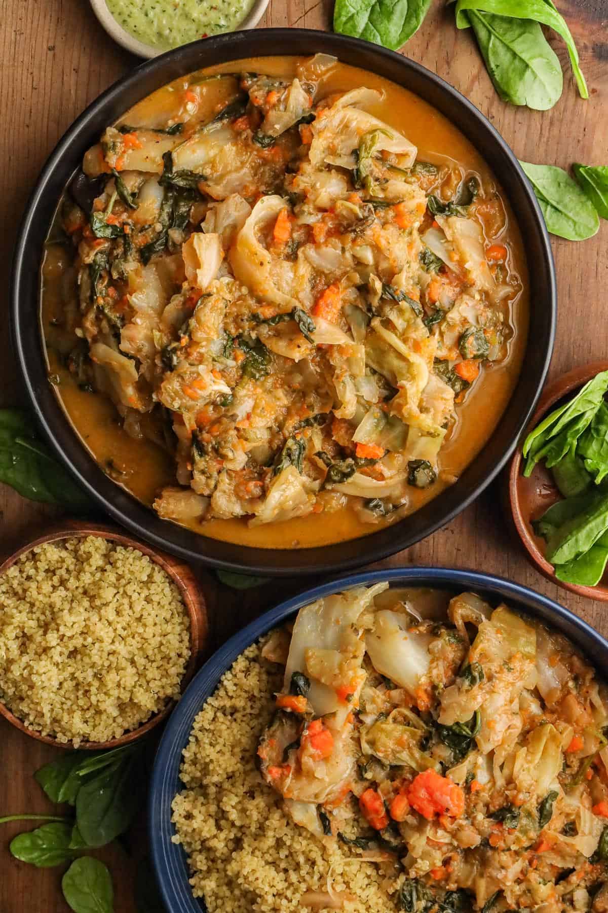 Haitian legume in black bowl, with quinoa and spinach on the side on a wooden board.