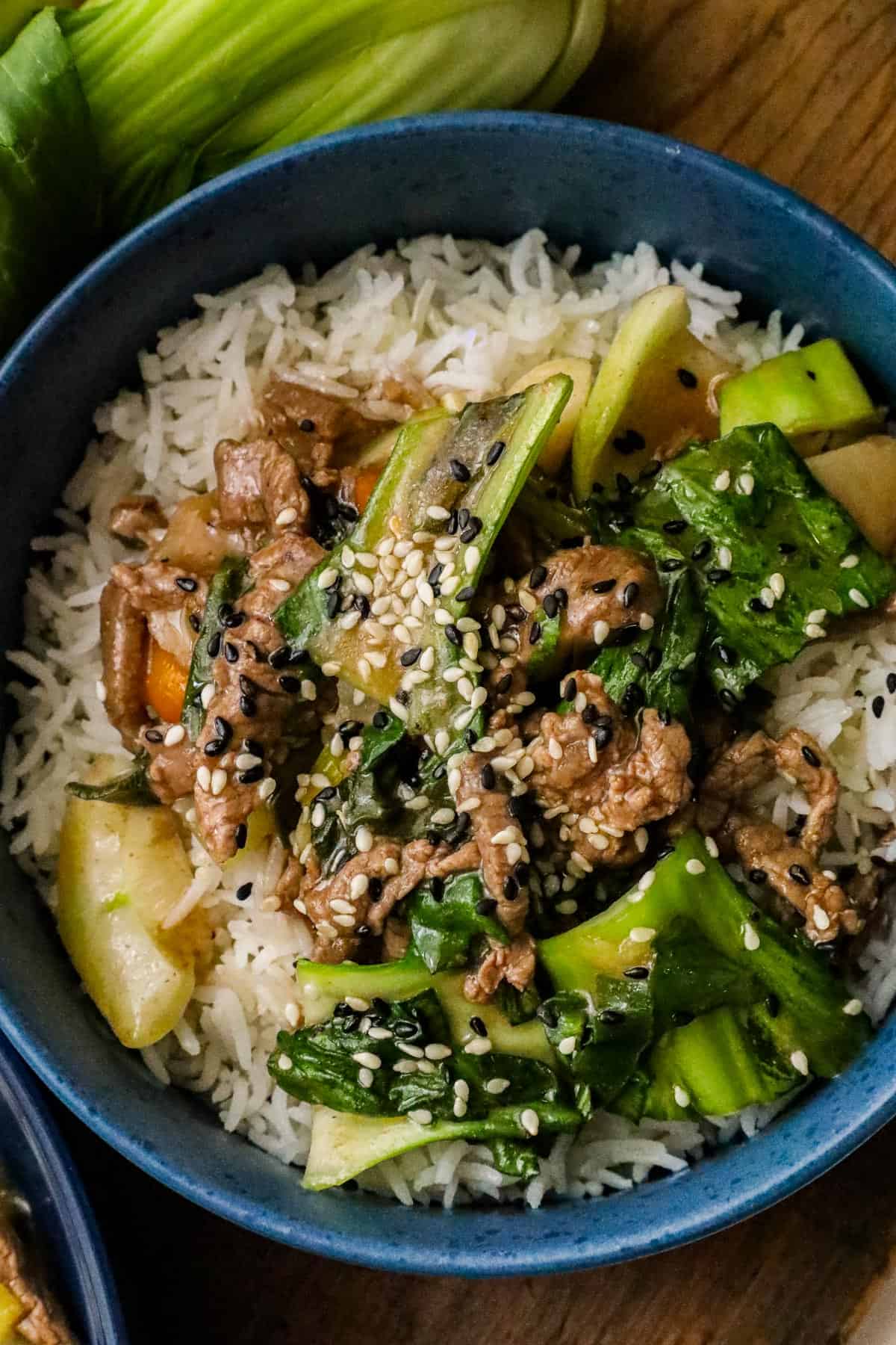 Beef Bok Choy recipe in blue bowl over a bed of white rice and sprinkled with sesame seeds.