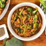 Chicken and broccoli stir in a white bowl with broccoli, fresh broccoli, and kitchen towel
