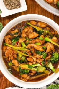 Chicken and broccoli stir in a white bowl on wooden cutting board