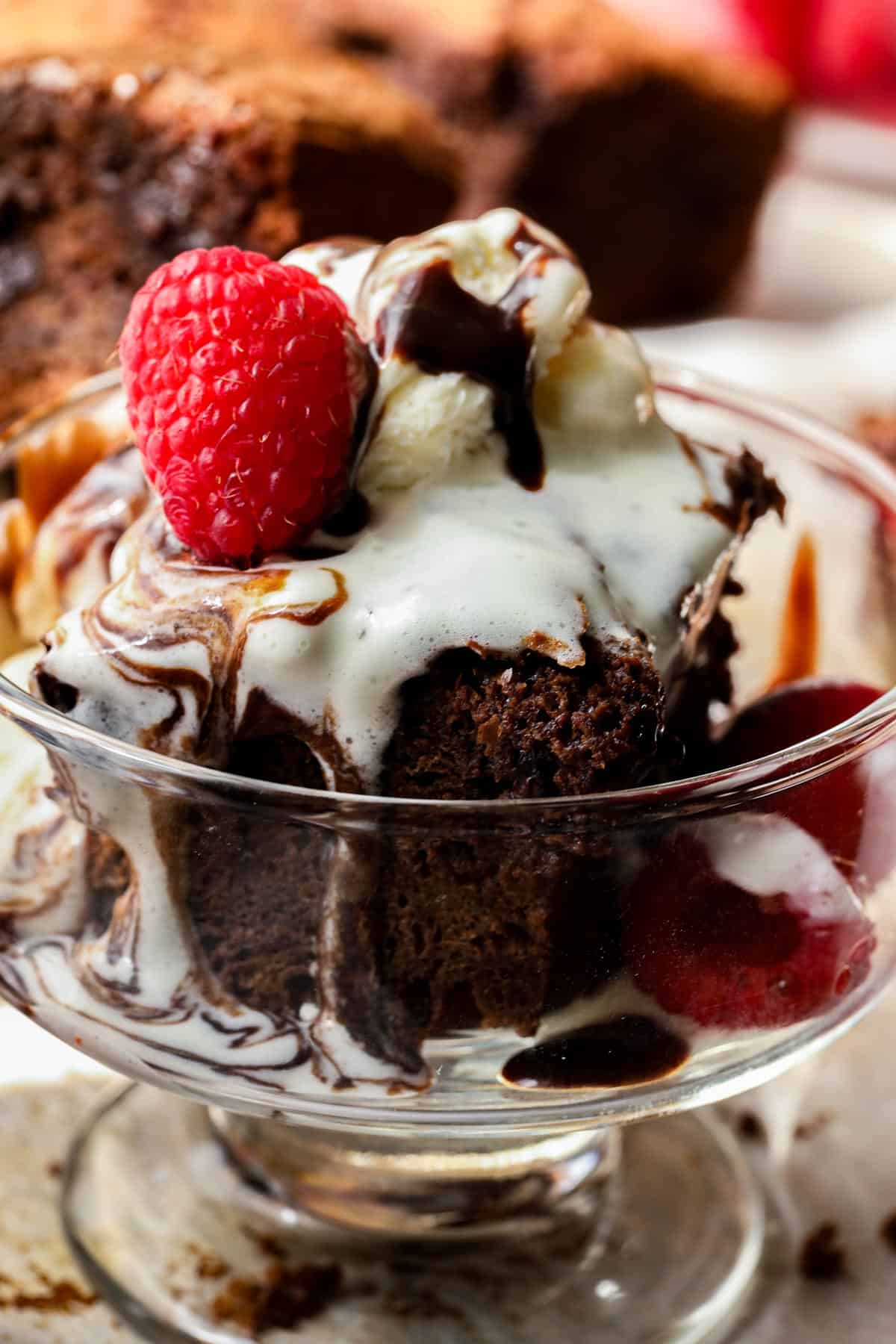 chocolate fudge brownies topped with ice cream and raspberry in glass dish.