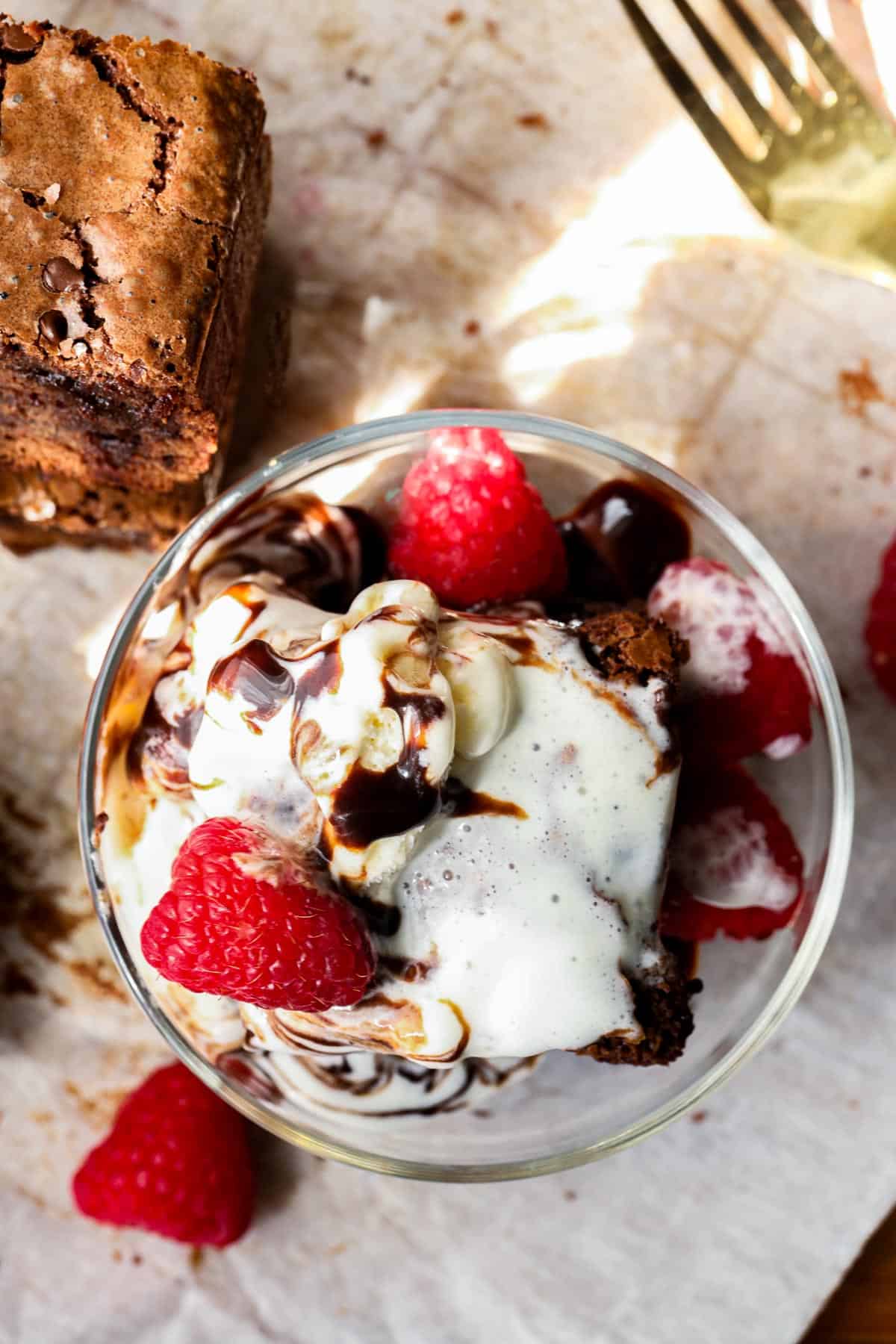 top view of chocolate fudge brownies topped with ice cream and raspberry in glass dish.