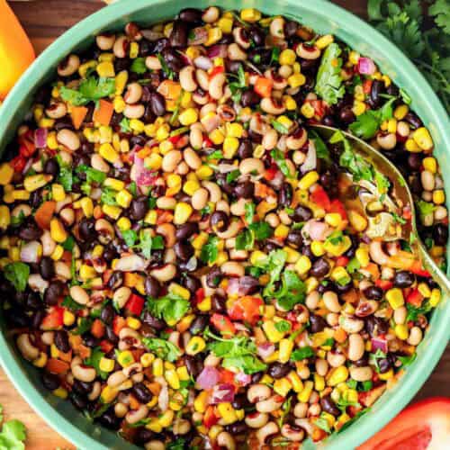 Cowboy Caviar in green bowl with chips, bell pepper cut in half, cilantro, and lime on the side