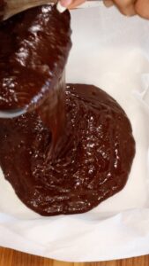 pouring chocolate fudge brownies mixture into parchment paper dish.
