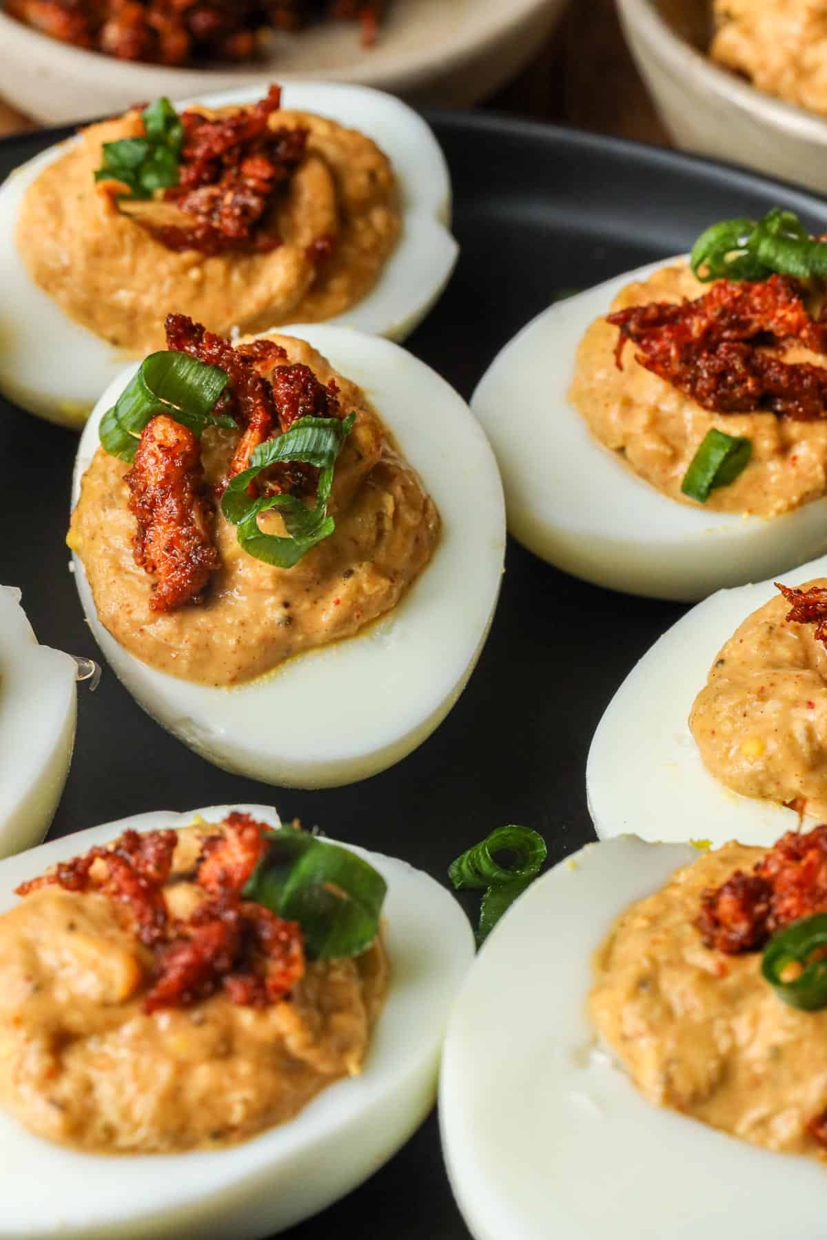 deviled eggs with crab meat topped with chives on a wooden board