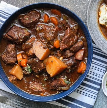 slow cooker beef stew in blue bowl with kitchen towel underneath.
